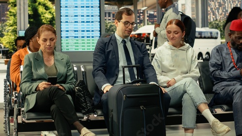 Bild auf Leinwand Young couple waiting in crowded bus terminal before long-haul interstate journey, man and woman with luggage and carry-on bags check departure board screen