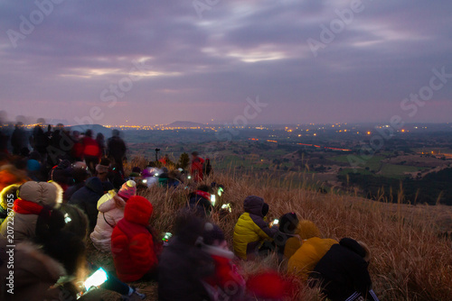 фотографія People gathered on a grassy hill watching a distant city light up at dusk