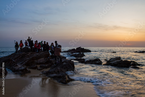 Canvastavla Tourists gather on rocky shore to watch the sunrise over the ocean