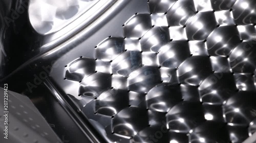 Stainless steel washing machine drum closeup. Dolly out shot revealing the interior of an empty washing machine, focusing on the shiny, metallic honeycomb texture of the stainless steel drum