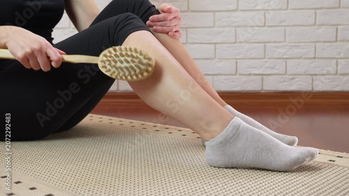 Woman performing dry brushing leg massage for cellulite reduction. Unrecognizable woman performing a therapeutic anti-cellulite massage on her leg with a wooden dry brush, improving circulation