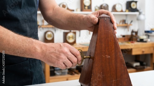 Clockmaker turning a brass key to wind a vintage wooden metronome on a workbench