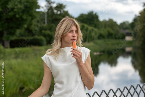 Woman holding an orange stick while standing near a river surrounded by trees in a park during daytime