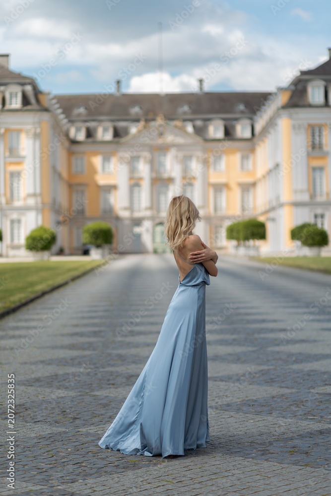 Obraz premium Woman stands on pathway in front of historic building wearing blue dress with arms crossed on a clear day