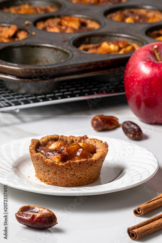 Mini apple pie tart with more cooling in a muffin tin in behind.