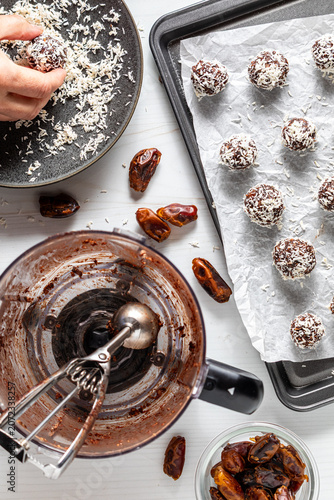 A hand rolling an energy ball in shredded coconut with ingredients around.