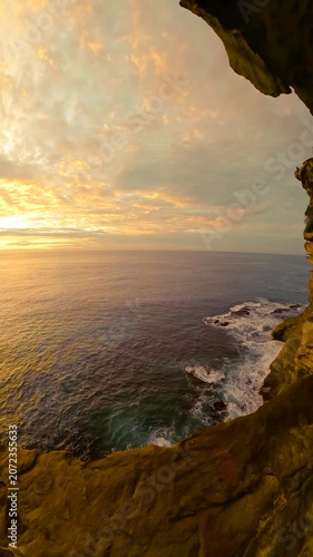 Fisheye video of sunrise over the ocean along the Sydney coastline, with calm water and rugged coastal cliffs glowing in soft golden morning light, Australia.