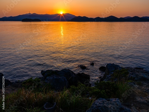 Fotografie Dramatic sunrise over the mountains and sea with golden sun reflection on water