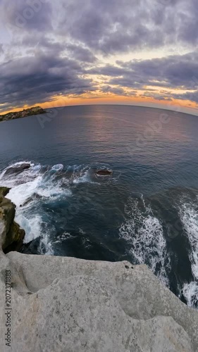 Slow motion fisheye video of Bondi Beach viewed from a coastal lookout at sunset, with calm ocean water, soft golden light, and the Sydney coastline, Australia.