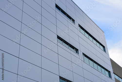 The exterior wall of a contemporary commercial style building with aluminum metal composite panels and glass windows. The futuristic building has engineered diagonal cladding steel frame panels.