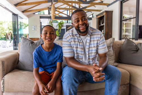 Vászonkép African American father and teen son sitting on sofa in living room facing foldi