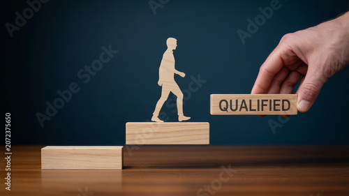 Hand placing block with qualified text near wooden figure climbing stairs symbolizing career success with professional achievement advancement