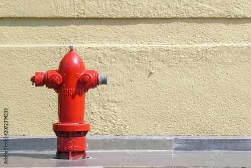 Konstfotografi Bright red fire hydrant on concrete sidewalk against textured yellow wall, safet
