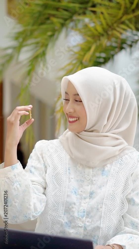 A young Asian Muslim woman is holding a gold bar. She looks very happy and joyful.