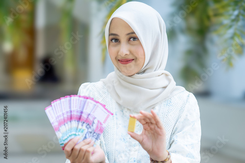 A young Asian Muslim woman is holding a gold bar. She looks very happy and joyful.