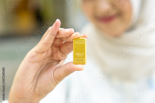 A young Asian Muslim woman is holding a gold bar. She looks very happy and joyful.