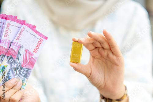 A young Asian Muslim woman is holding a gold bar. She looks very happy and joyful.