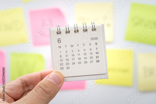hand holding small desk calendar for June 2026 with colorful sticky notes background. business planning, appointment scheduling, project milestones, team collaboration, and time management strategies.
