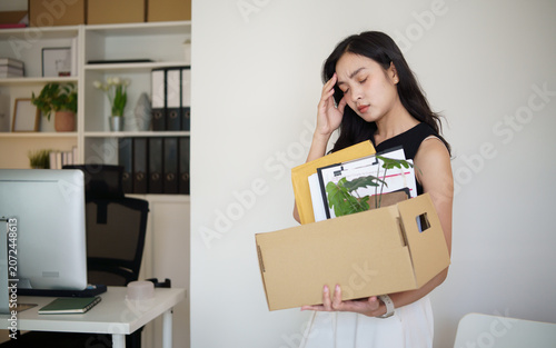 Fotografía Unemployed woman packing office belongings into a cardboard box after losing her job, looking stressed at her desk