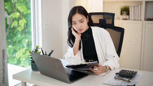 Fotografie Businesswoman reviewing financial documents and looking worried while working on laptop in home office