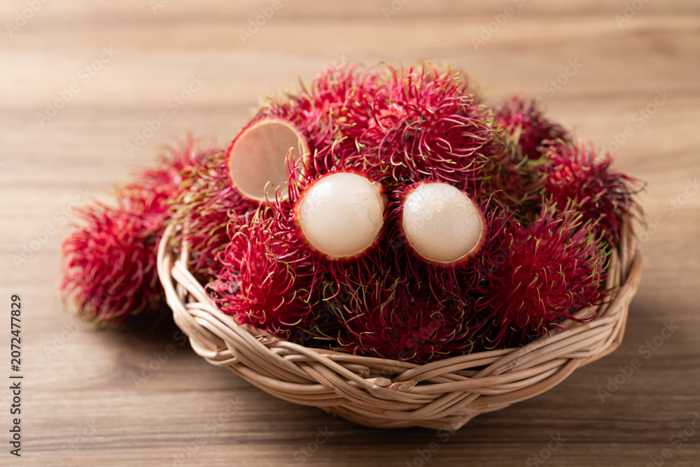 Fototapeta premium Fresh rambutan fruit in a wicker basket on wooden background, Tropical summer fruit in Thailand