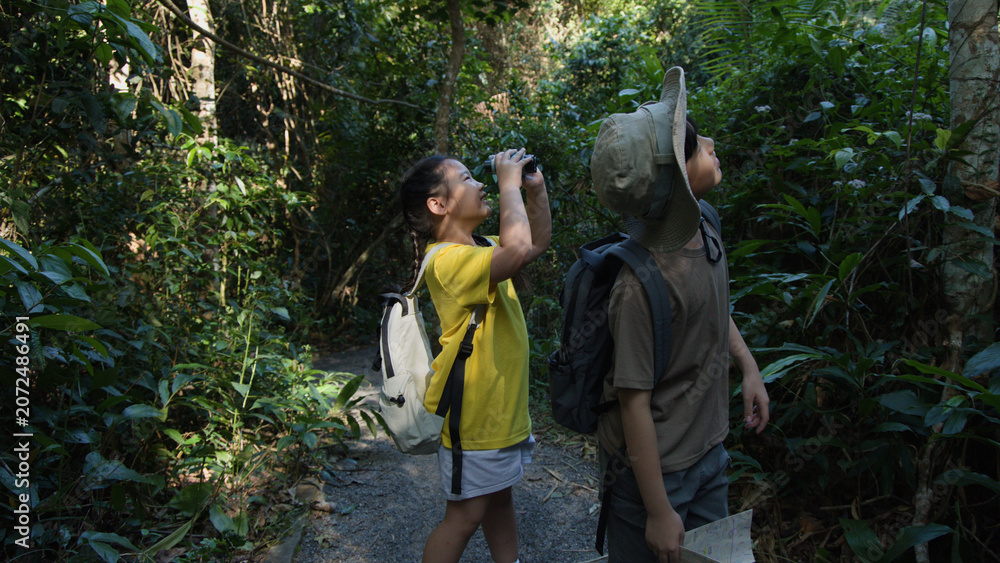 Naklejka premium Two Asian Children Using Binoculars While Hiking in Tropical Forest