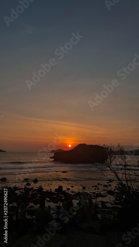 Golden sunset over a rocky coastal shoreline with gentle ocean waves and silhouetted cliffs, creating a tranquil seascape at dusk
