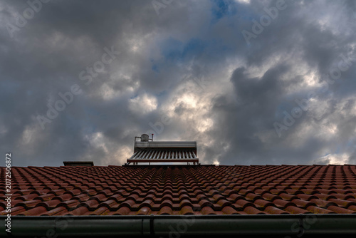 Dirty solar water heater boiler on rooftop on a cloudy early summer morning.