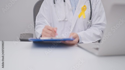 Professional doctor using laptop and taking report notes on notebook for Yellow Ribbon concept of yellow September, Suicide prevention day, Childhood, July Sarcoma, bone and bladder cancer