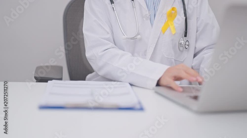 Professional doctor using laptop and taking report notes on notebook for Yellow Ribbon concept of yellow September, Suicide prevention day, Childhood, July Sarcoma, bone and bladder cancer