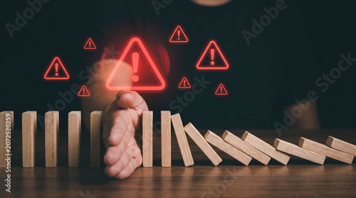 A hand stopping falling wooden dominoes to represent effective risk management and preventing corporate business failure