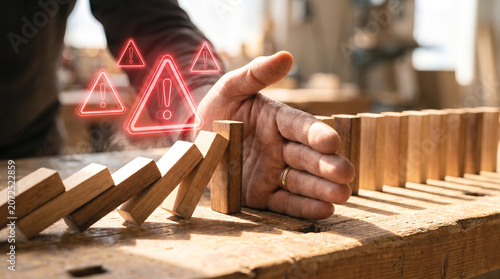 A hand stopping falling wooden dominoes with warning signs representing effective business risk management and crisis prevention
