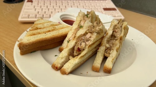 A delicious, freshly prepared chicken sandwich served at a clean modern office workspace with a sleek computer keyboard softly blurred in the background.