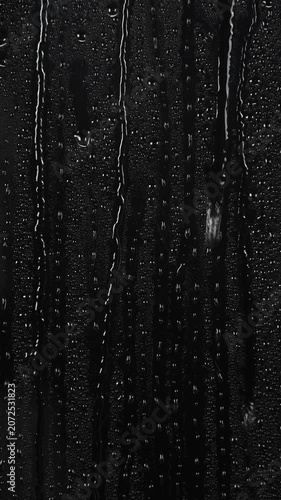 water drops flow down the surface of glass on black background.	