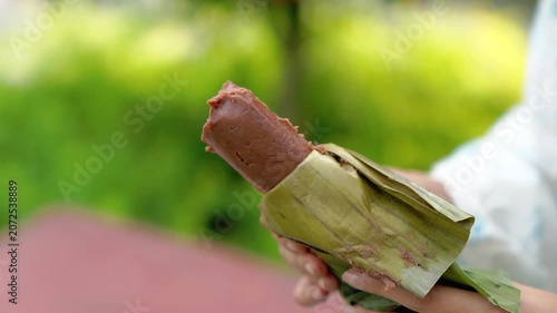 A young Asian Muslim woman is enjoying getuk pisang, a specialty food from Kediri, Indonesia, made from mashed steamed bananas wrapped in banana leaves.