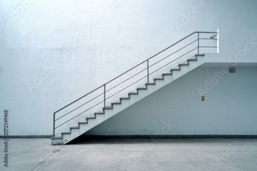 A concrete staircase with metal railings ascends against a white wall.