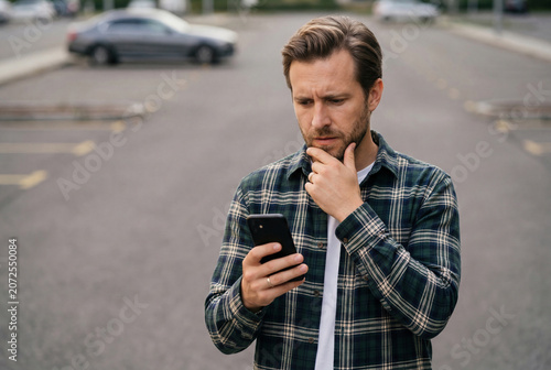 Thoughtful man looking at his smartphone in a parking lot