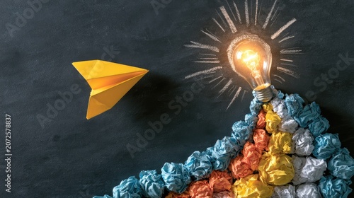 Yellow paper airplane flies towards bright lightbulb emerging from crumpled paper