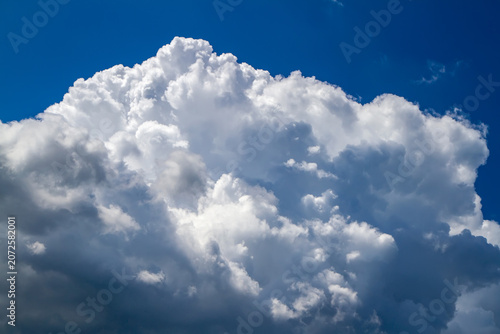 Large white cumulus cloud against deep blue sky. Meteorological weather phenomenon and nature background. Concept of freedom, peace and clear atmosphere.