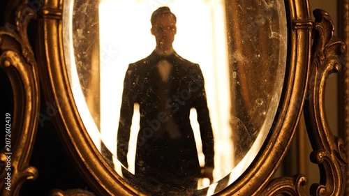 A dark silhouette reflects in a dusty vintage gold mirror