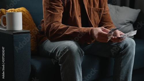 Close-up of an unrecognizable man counting dollars while sitting on a sofa at home