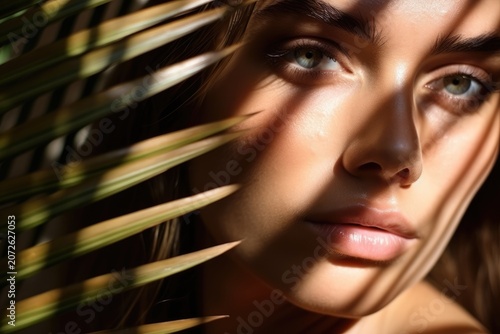 Close-up portrait of a young woman with palm leaf shadows across her face in warm sunlight