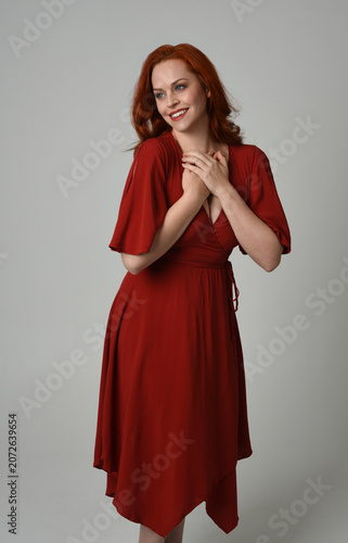 portrait of beautiful model with long red hair, wearing an elegant red vintage dress. standing pose,  isolated silhouette figure on studio background.