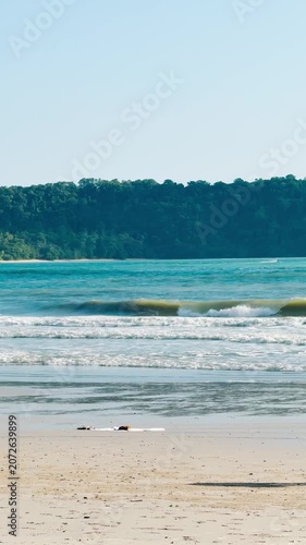 4K Vertical shot of ocean waves at Pantai Cenang Beach, Langkawi Island, Malaysia. Waves crashing at shore. Summer vacation and holidays concept. Tropical beach background.