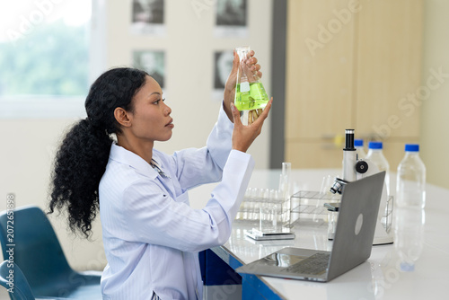 African American female scientist working with microscope and notebook computer in laboratory