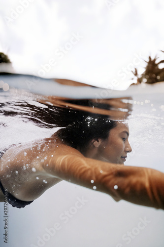 A peaceful young woman glides gracefully underwater beneath the surface, capturing a sense of calm and freedom in an aquatic environment. Generative AI.