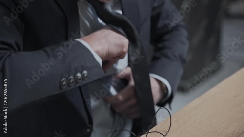 Person puts the microphone through his shirt and attaches it to his jacket. TV presenter or journalist is preparing to go on the air. Man in a business suit is sitting at a table.