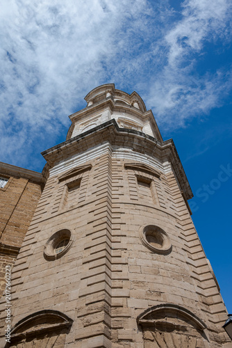 Low-angle view of the Levante Tower (Clock Tower) of Cádiz Cathedral, Spain, showcasing its baroque architecture against a deep blue sky.