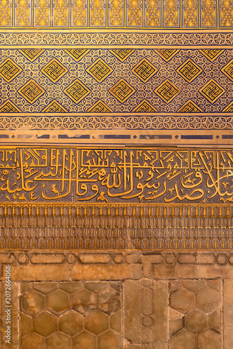 Ornate golden calligraphy and geometric tilework inside Gur-e-Amir mausoleum in Samarkand. Layered bands of Arabic script, painted patterns, and onyx panels showcase Timurid decorative artistry.