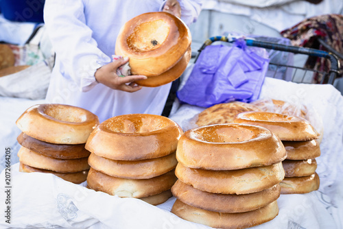 Heap of glossy golden hot round tandoor-baked breads with sesame seeds on vendor stall.  Siab bazaar in sunny day, street food market. Traditional bread naan in asian. Samarkand, Uzbekistan.